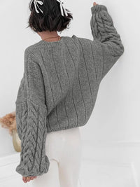 Back view of a model wearing a gray cable knit long sleeve sweater, showcasing its stylish, oversized fit.