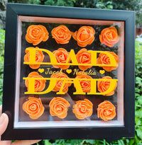 a person holding up a framed picture of orange roses