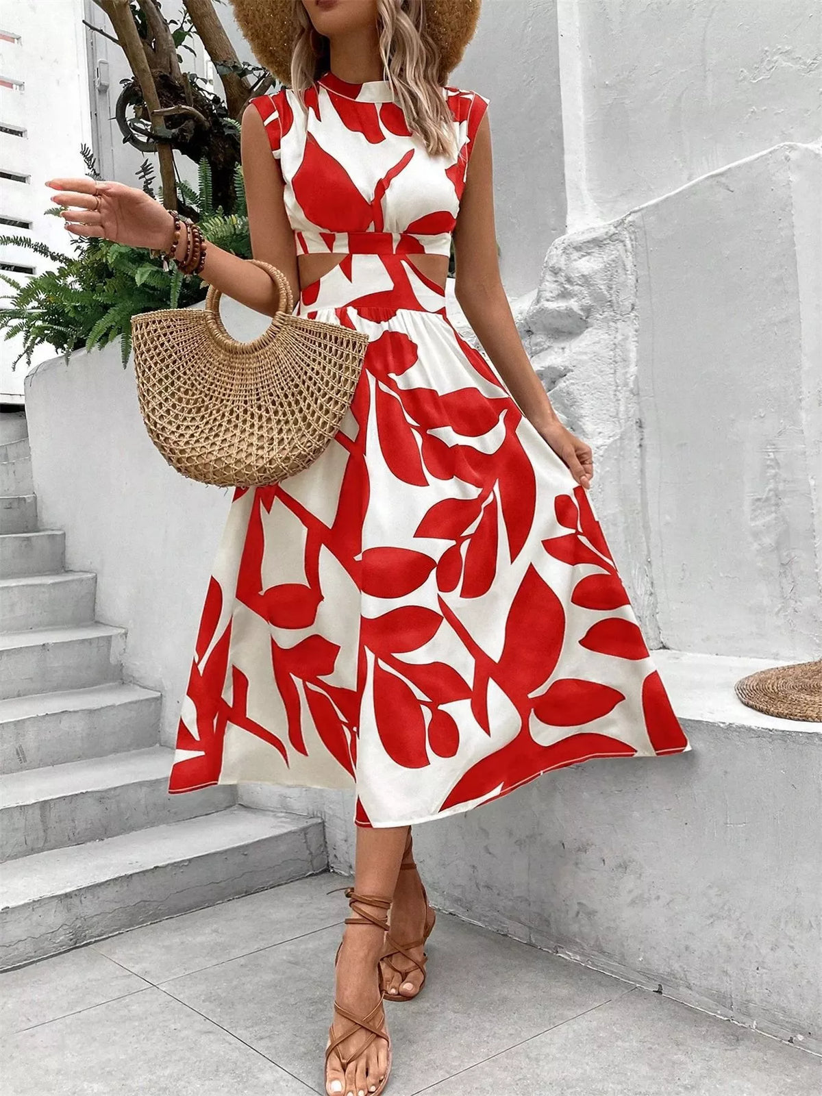 Cutout printed sleeveless dress featuring red leaf patterns, styled with a straw bag and heels, ideal for summer outings.