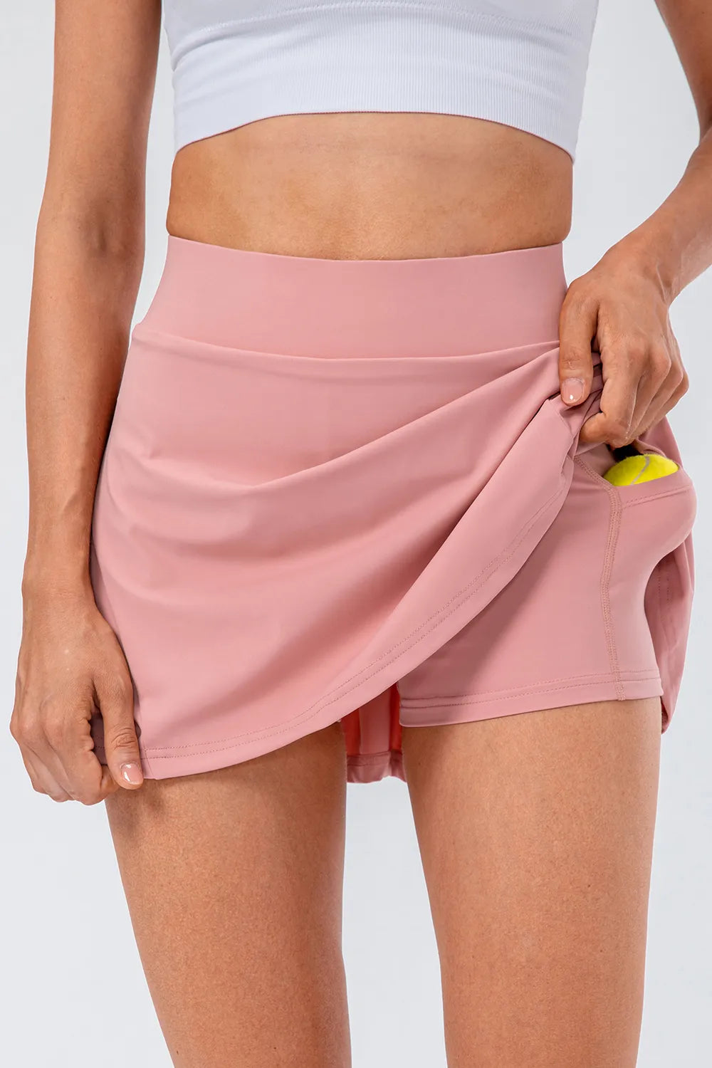 Model showcasing the High Waist Pleated Active Skirt in pink, featuring a hidden pocket and stretchy fabric.