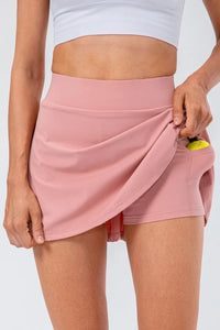 Model showcasing the High Waist Pleated Active Skirt in pink, featuring a hidden pocket and stretchy fabric.