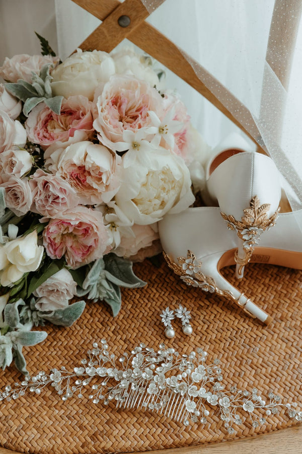 Bouquet of flowers, high-heeled shoes with decorative elements, and jewelry on a textured surface.