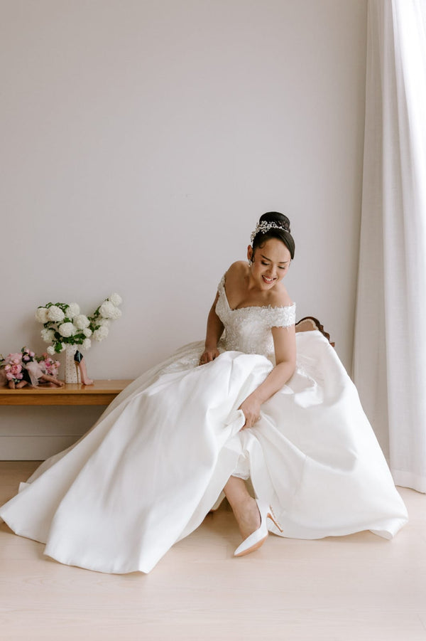 Woman in a white wedding dress sitting on a chair with a neutral background